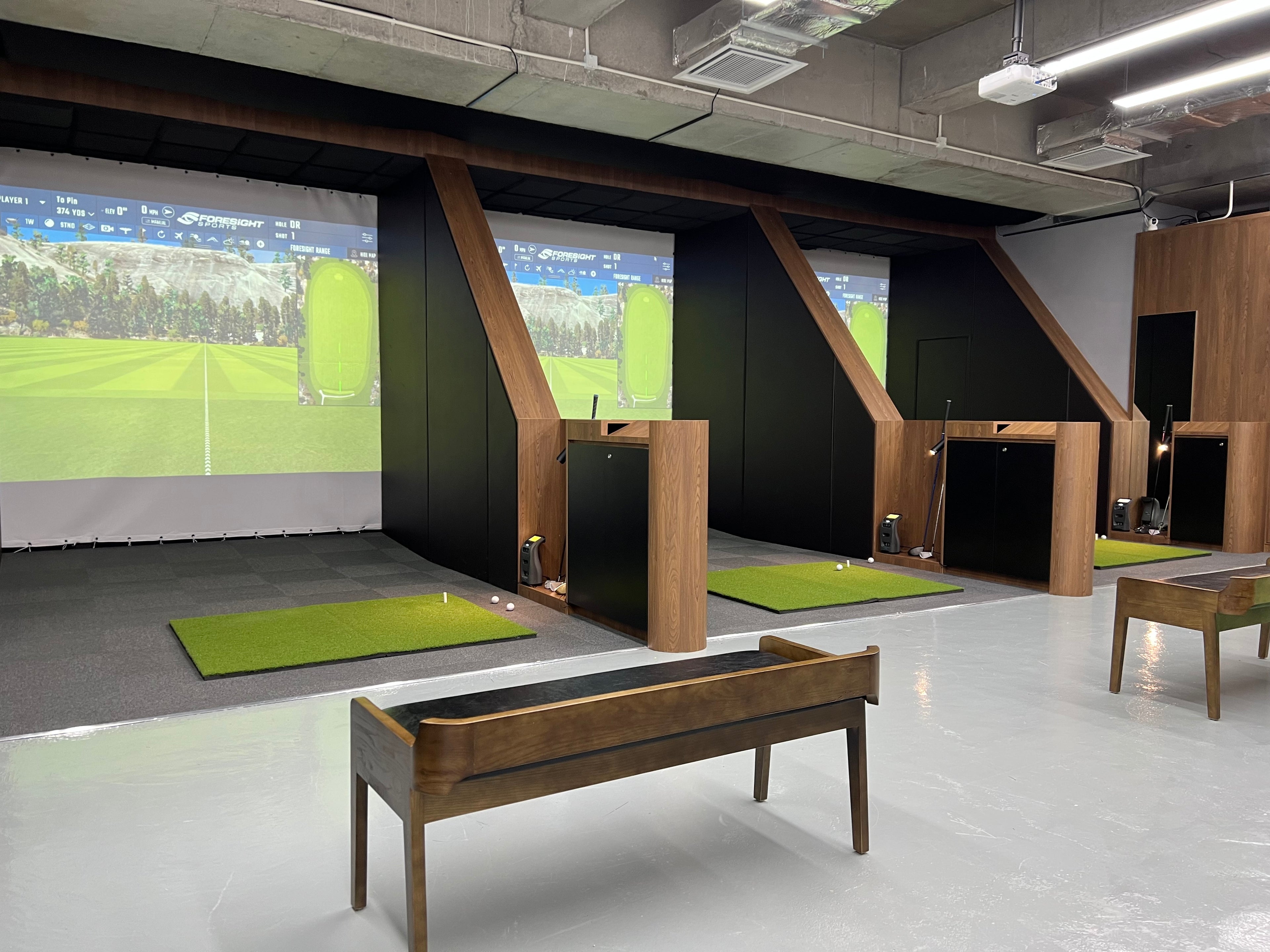 Image of three indoor golf simulator bays. Each simulator bay features a high-quality screen, a golf mat, and a high speed camera.